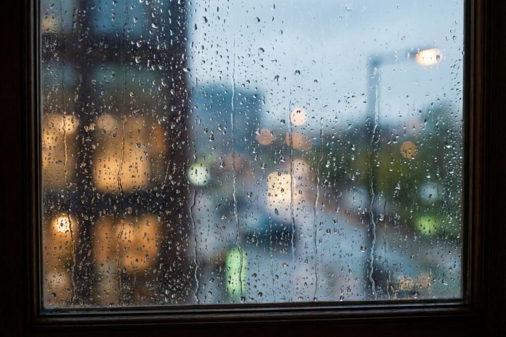 雨粒が滴る窓越しに滲む街の灯りと、止まった時間を象徴する静止画