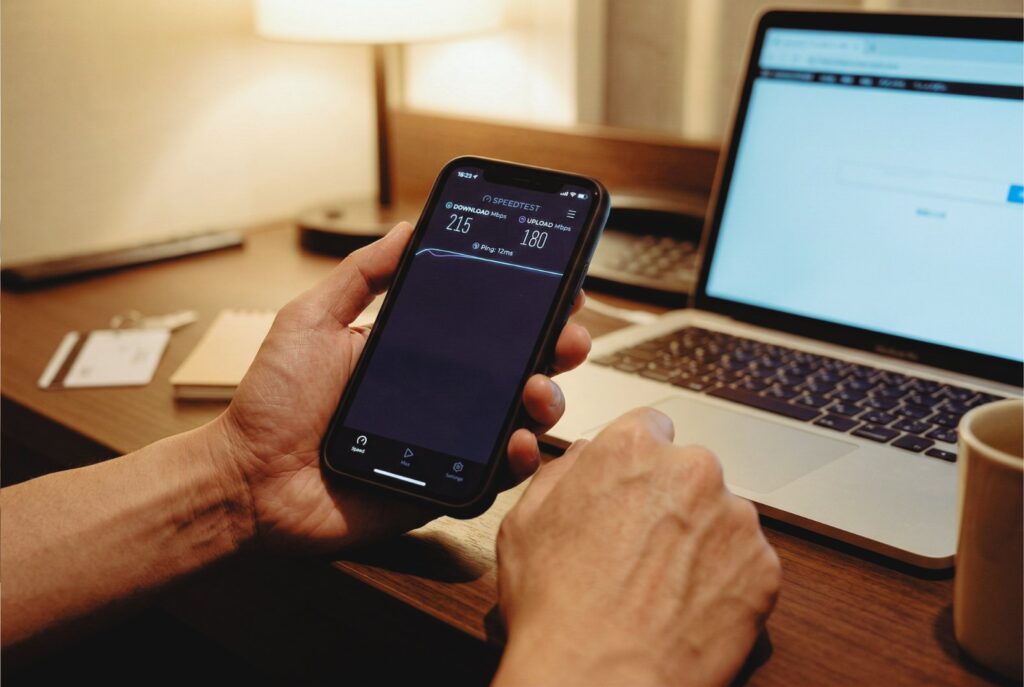 夜のホテルデスクでスマホのスピードテスト画面を見つめる日本人男性の手元。